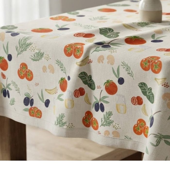 A tablecloth printed with the Pasta Love tomato, olive and basil repeat, draped over a table.